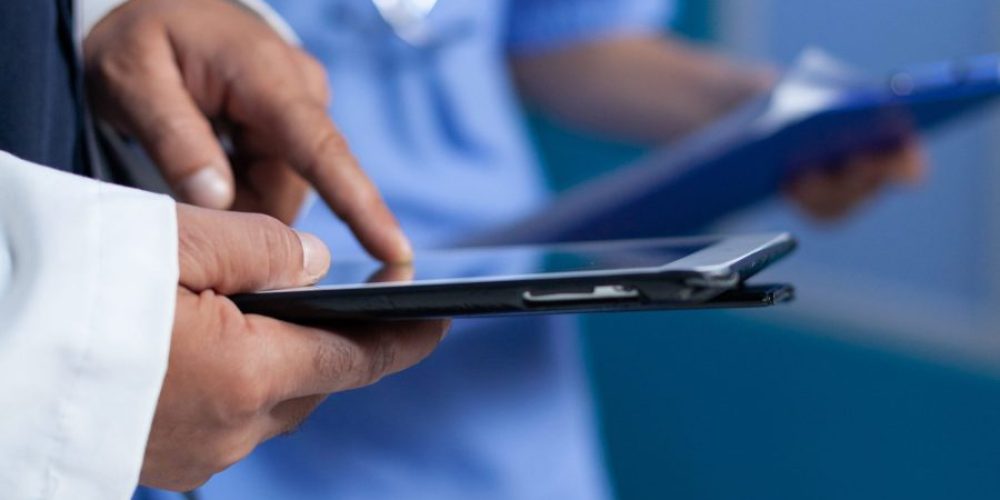 Close up of medic pointing at tablet screen for medical practice, working late. Doctor using modern device with touch screen and talking to assistant about healthcare system overtime.