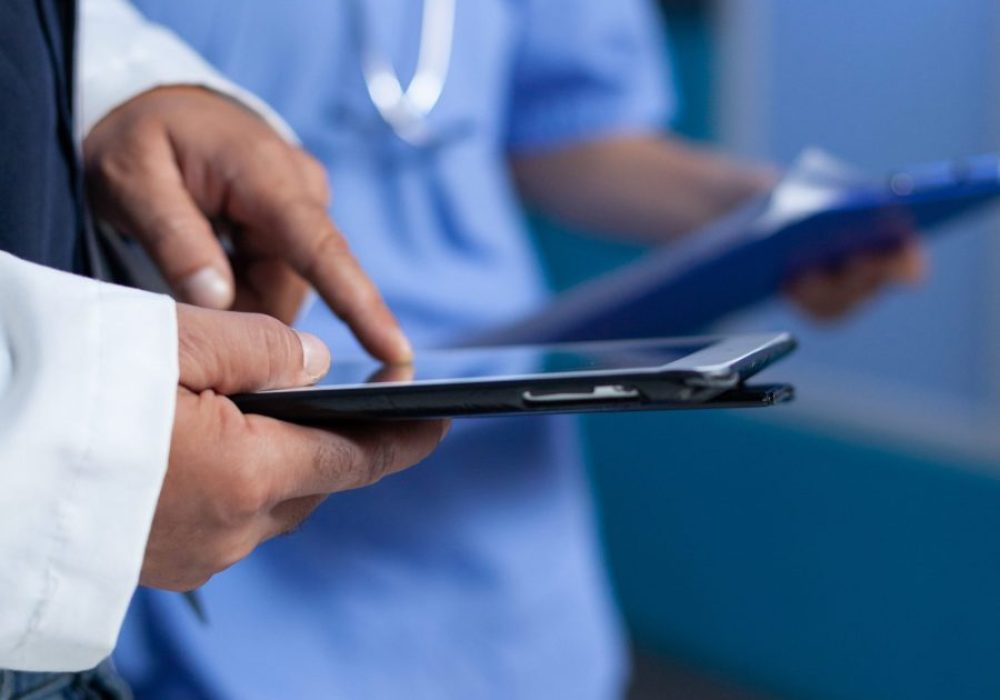 Close up of medic pointing at tablet screen for medical practice, working late. Doctor using modern device with touch screen and talking to assistant about healthcare system overtime.